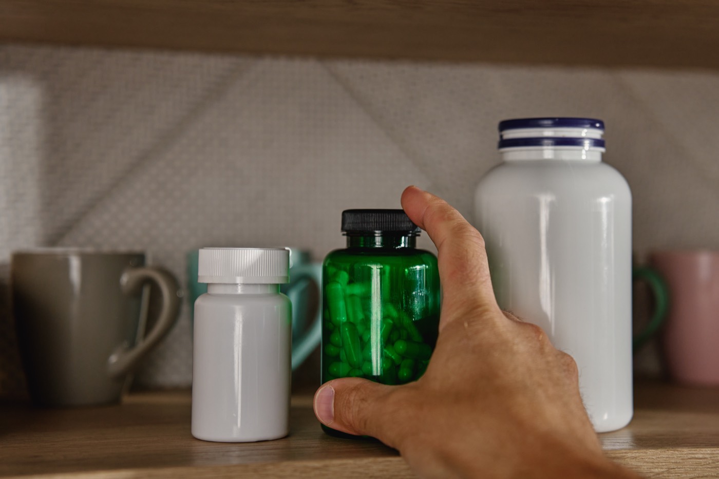 A hand reaching for a supplement tub at the back of a cupboard
