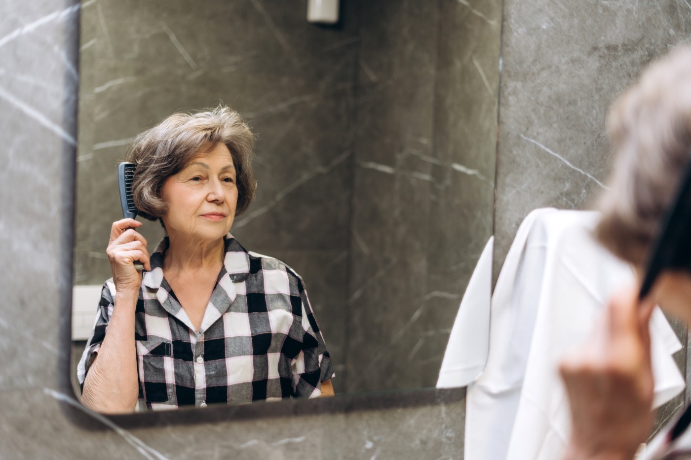 A woman brushing her hair in the bathroom mirror